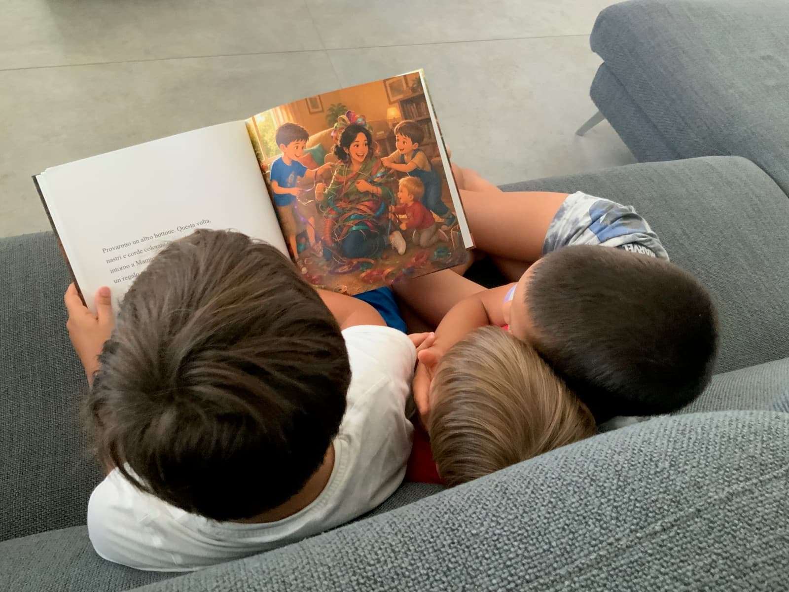 Tre bambini seduti sul divano che sfogliano insieme il loro libro illustrato
